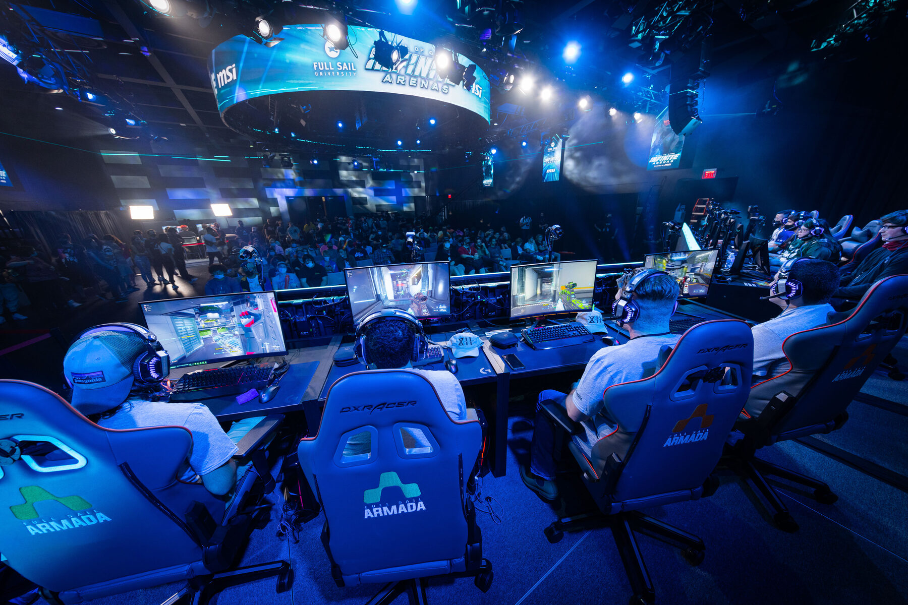 View from behind Armada players at their stations, facing the stage and the ring