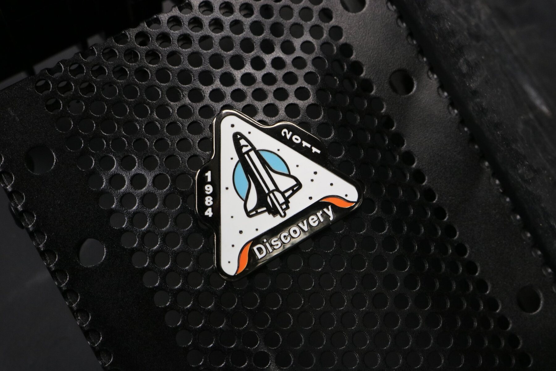 Discovery space shuttle enamel pin on perforated black metal