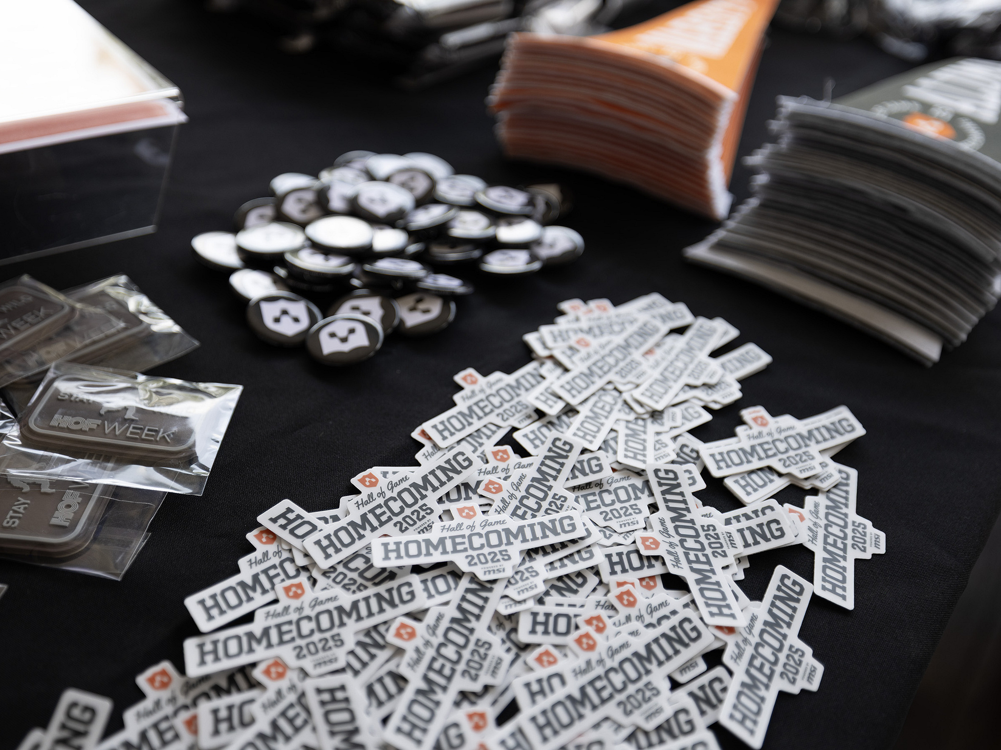 A table of Homecoming 2025 lockup stickers, shield buttons, pennants and HOF Week patches at the event