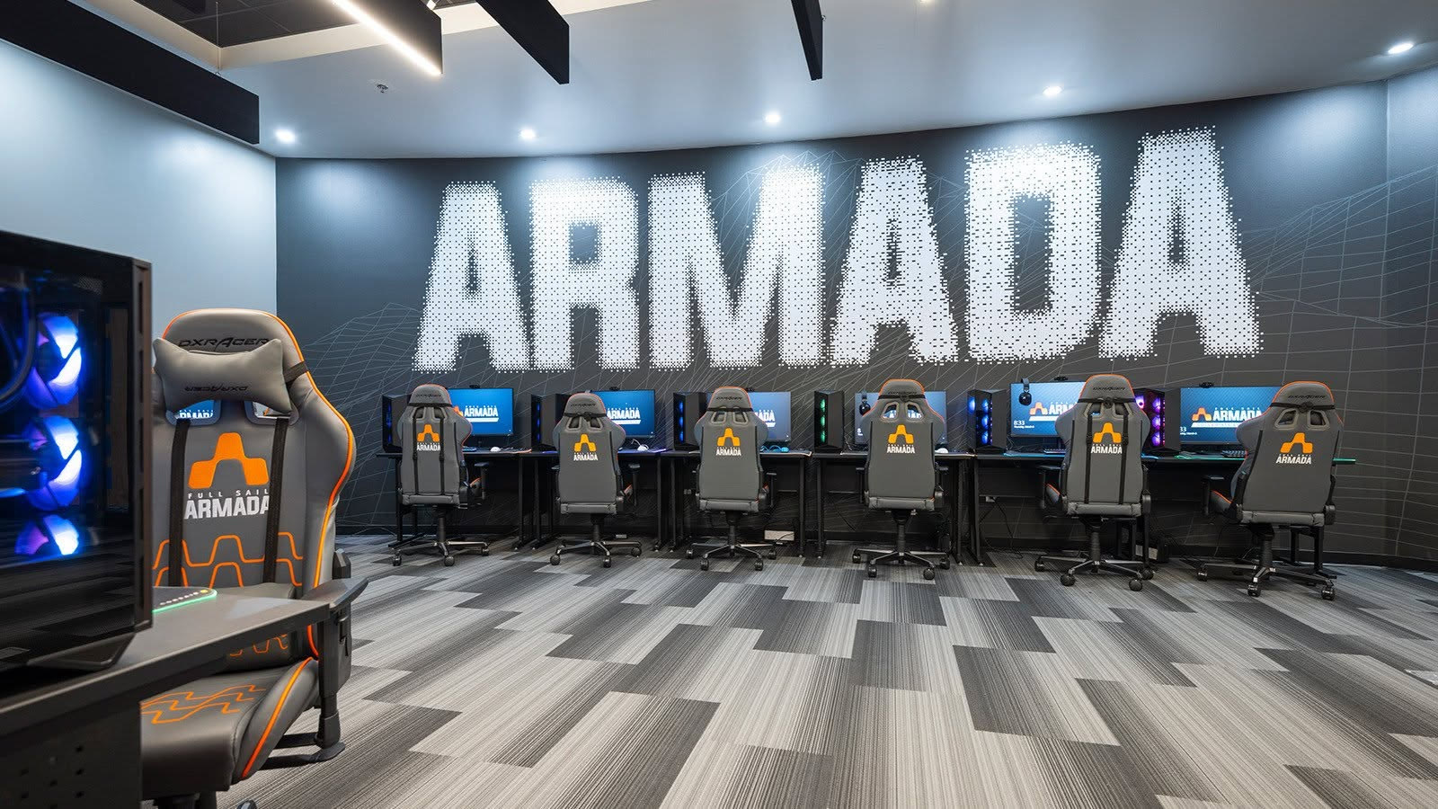 The back room: a large textured ARMADA wordmark across a curved wall above a row of gaming stations