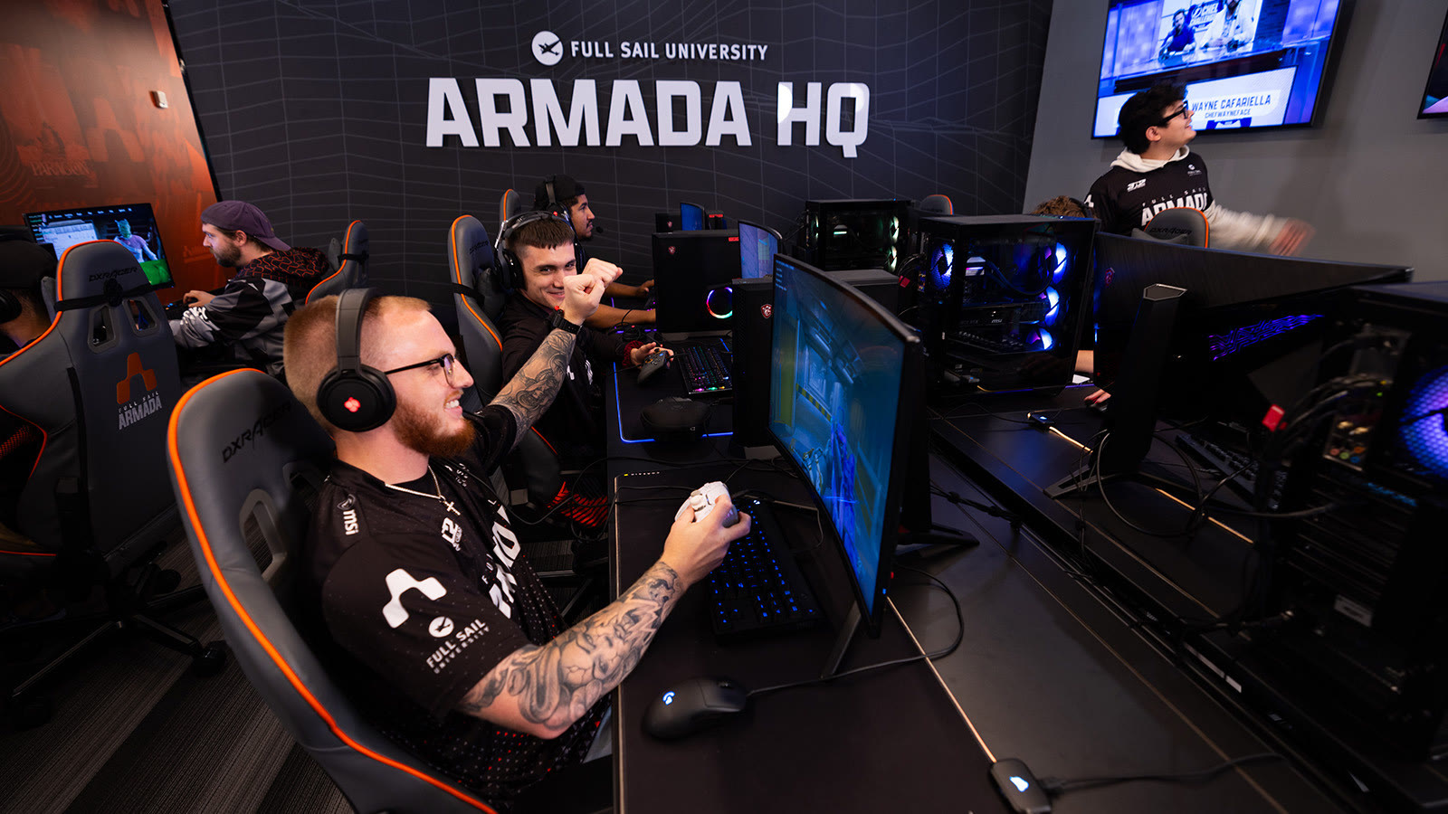Armada players competing, with the Armada HQ wall and a stream screen behind them
