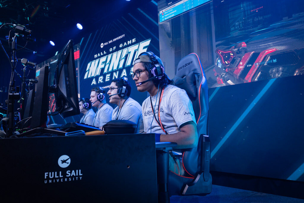 Players in headsets at their desk in front of the Infinite Arenas wall
