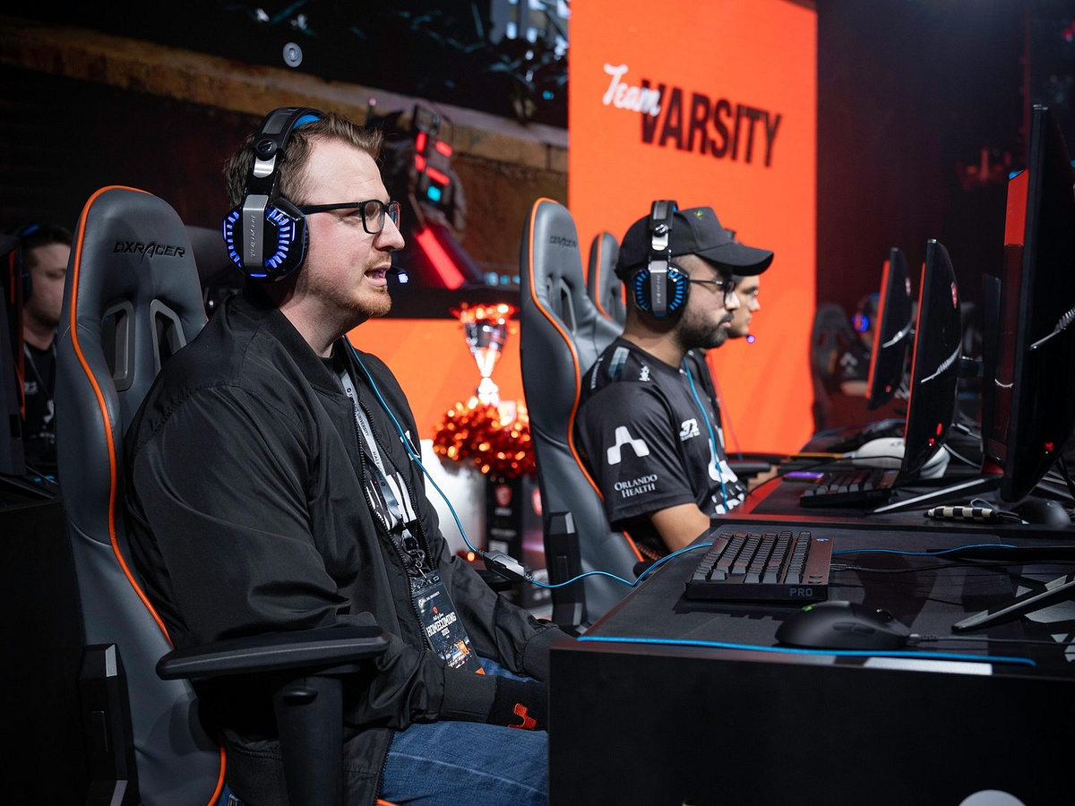A player in a headset at his station, with the Team Varsity screen and the Hall of Game trophy behind him