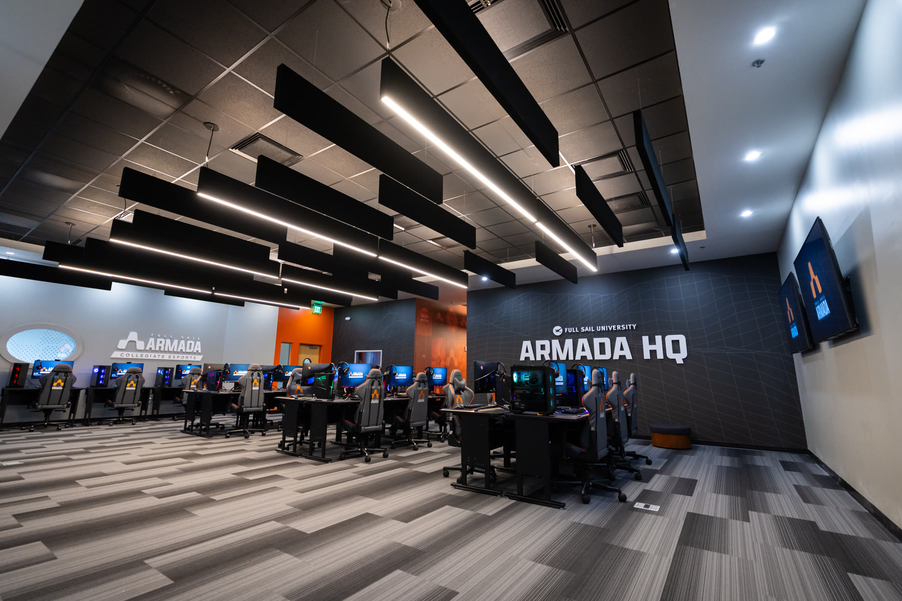 The Armada HQ main room: rows of gaming stations under a dark slatted ceiling, with the Armada HQ wall graphic and orange accent wall at the far end