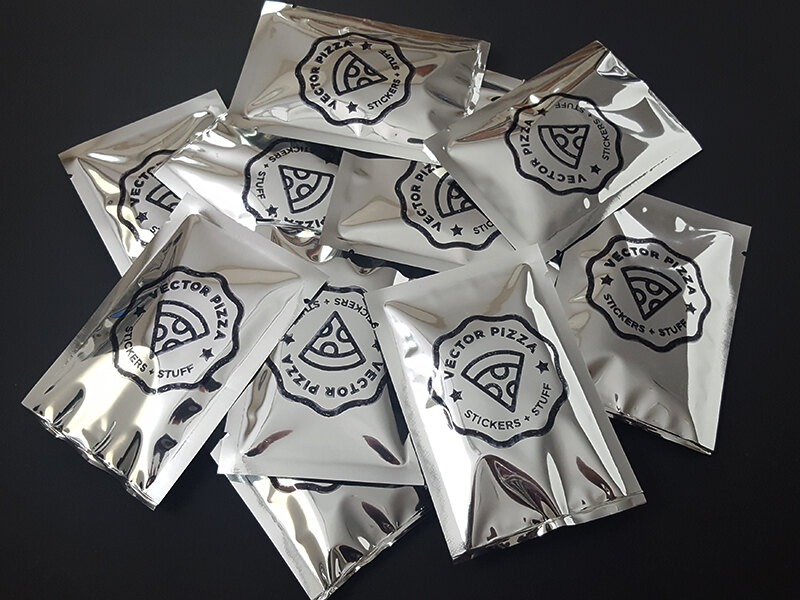 A pile of silver mylar bags hand-stamped with the Vector Pizza seal
