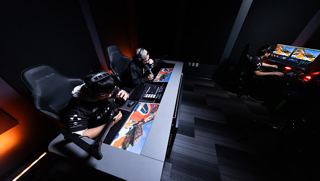 The caster room: two casters at a desk with mixing equipment, lit in orange and dark tones